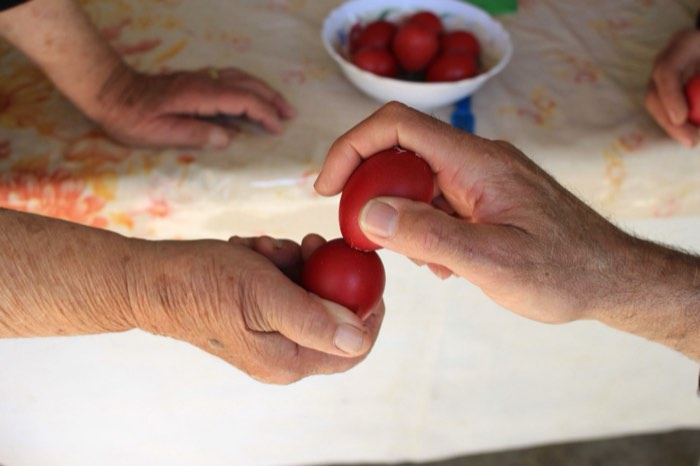 Close-up of hands tapping red-dyed Easter eggs together, the traditional Greek Orthodox Easter "tsougrisma" egg-cracking game.