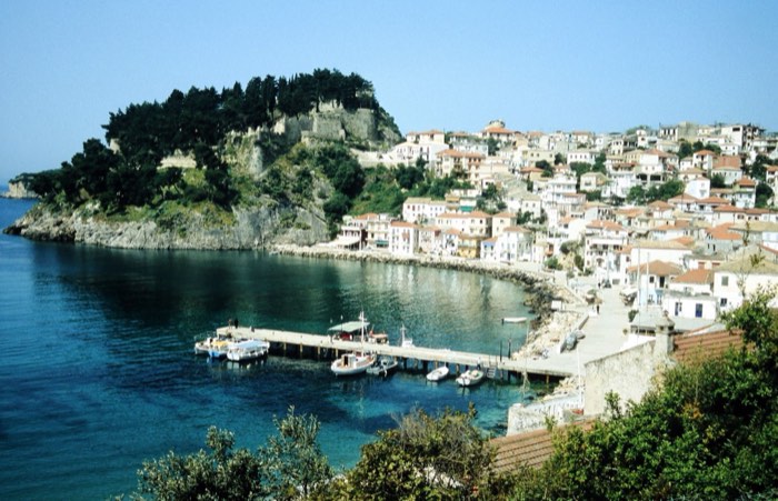 An elevated wide view of Parga, Greece, looking down over the harbour, whitewashed hillside houses and the fortress-topped promontory.
