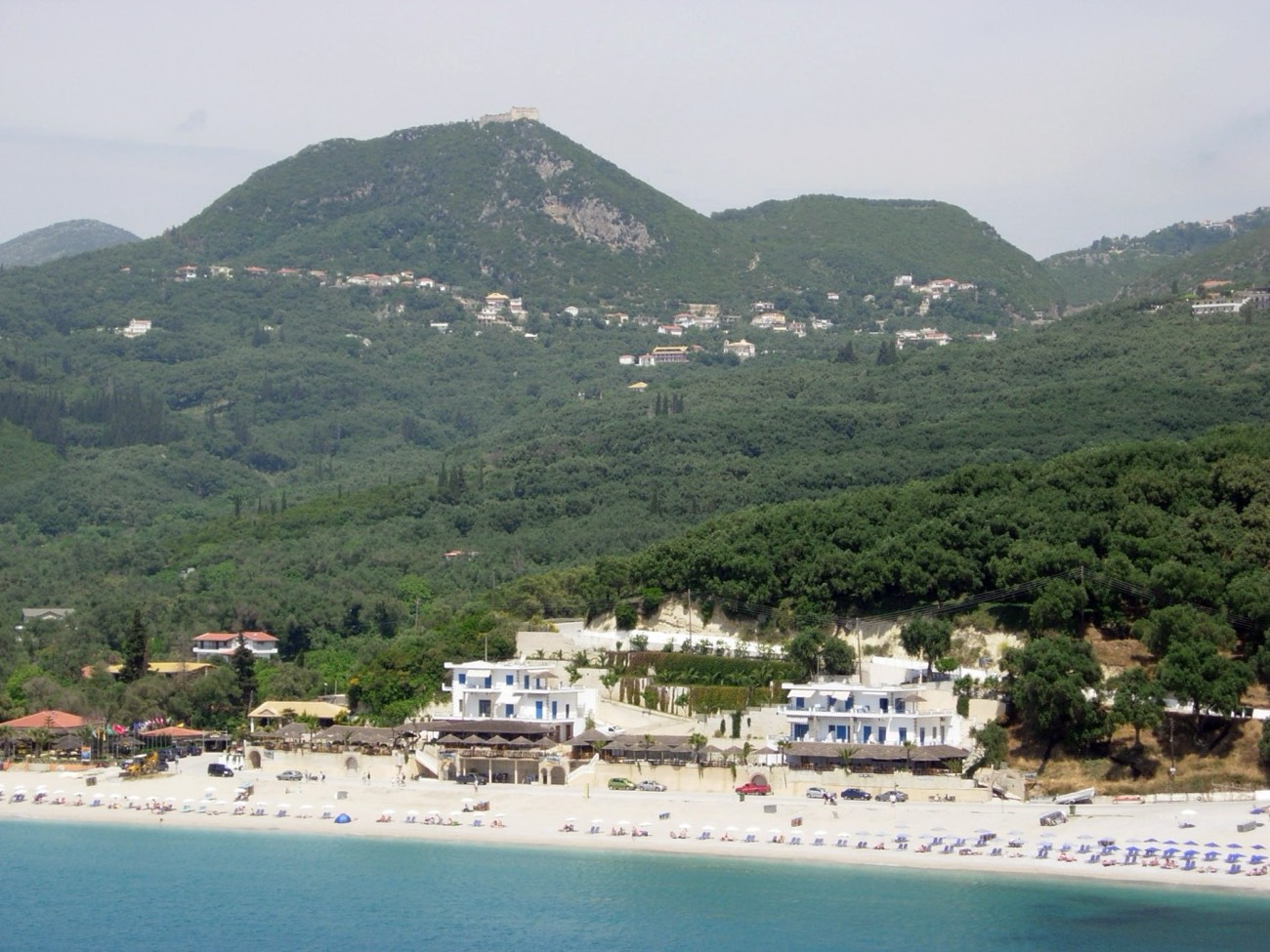 The photo shows Valtos beach at Parga, Greece, with the fortress of Ali Pasha (Parga Castle) visible in the background.
